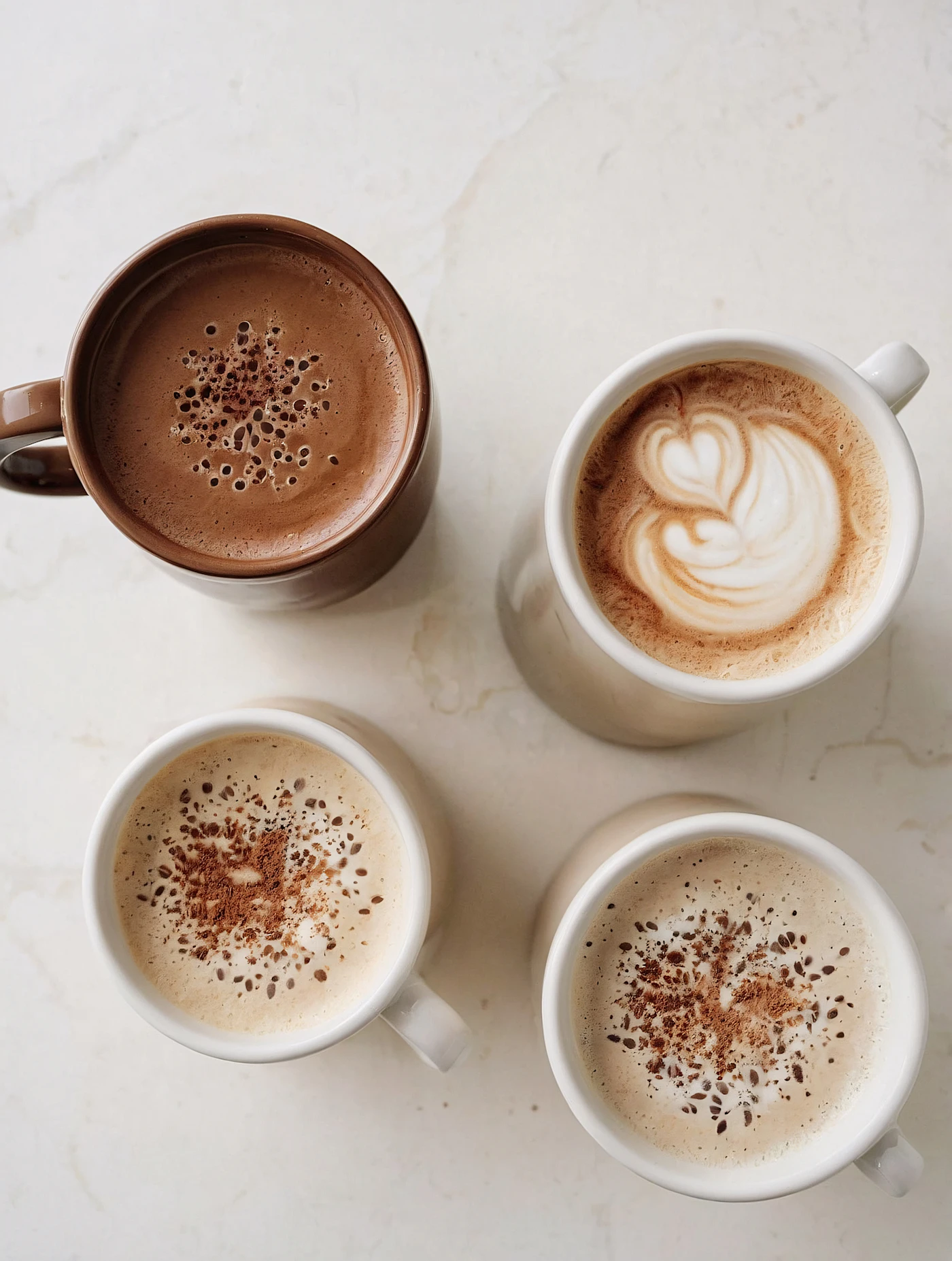 Four coffee drinks in ceramic mugs arranged on a marble table