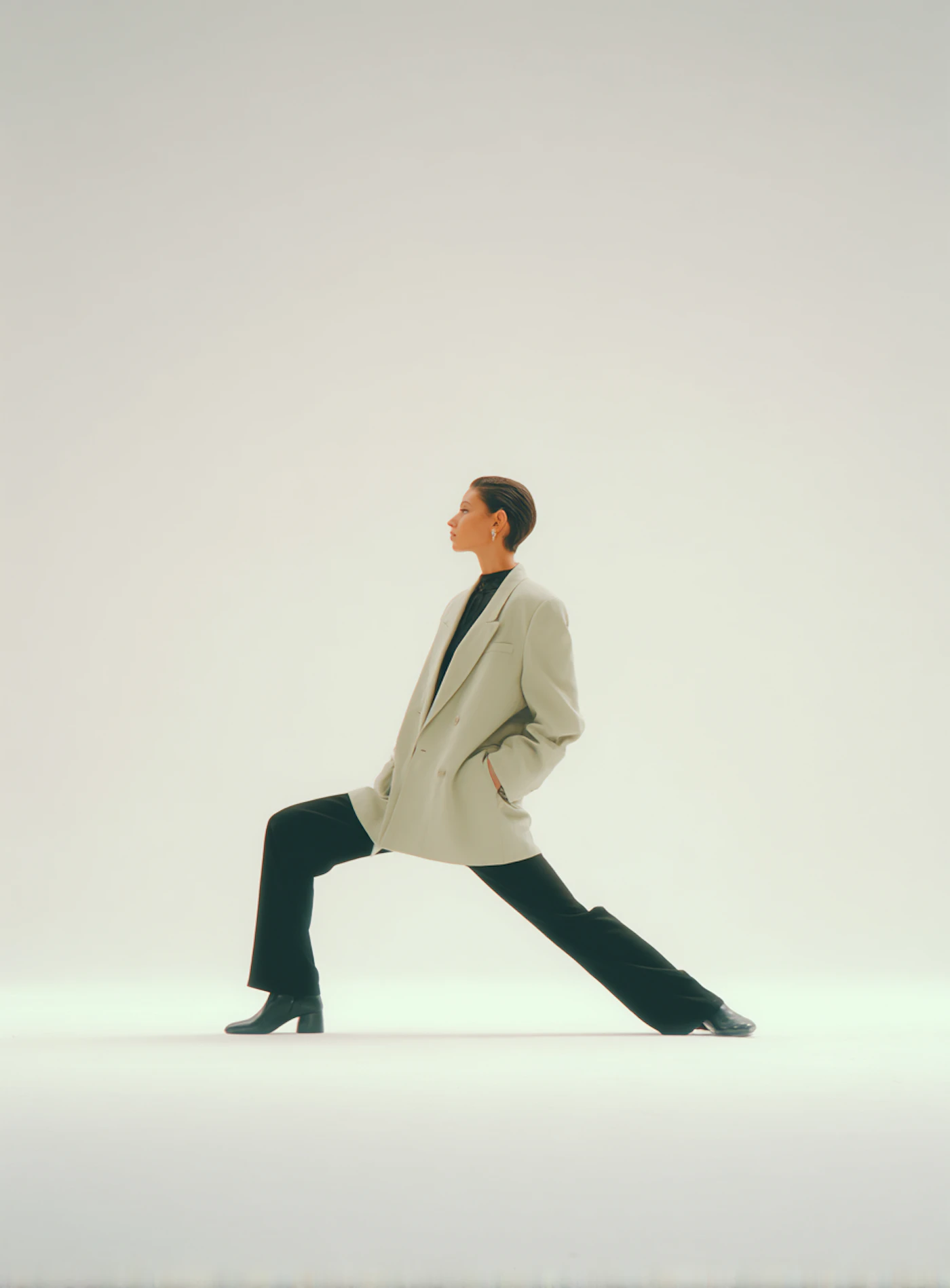A model in a pale blazer and black trousers posing against a white backdrop
